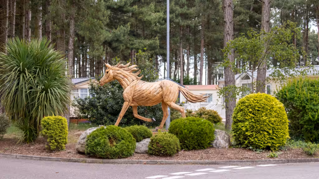 A wooden horse statue in the middle of bushes